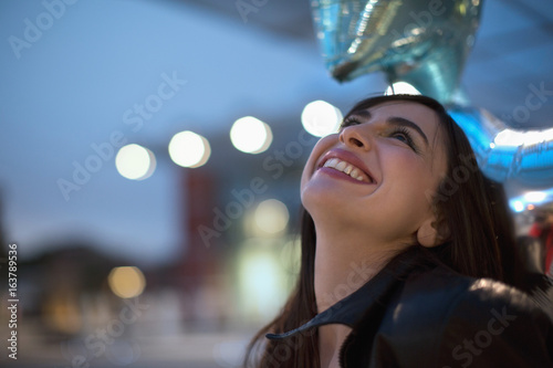 Beautiful young woman with shiny star balloons going out in the evening smiling