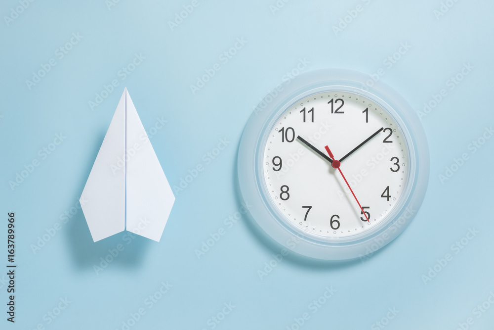 Flat lay of white paper plane and wall clock on pastel blue color background  Stock Photo | Adobe Stock