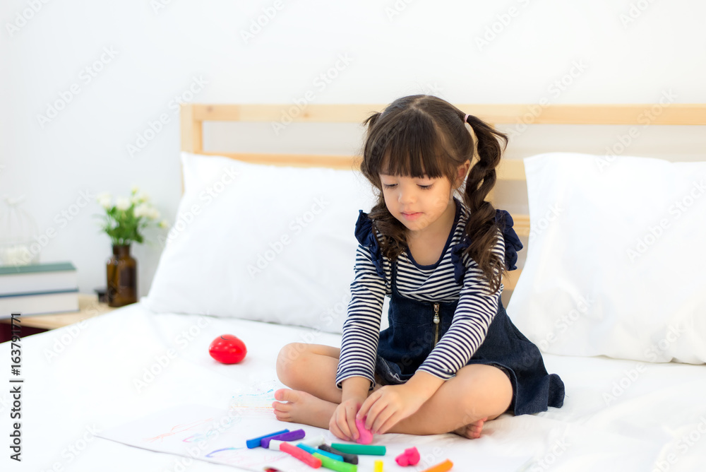 Funny happy toddler girl reading a book and playing with her toy teddy bear in bed. Kids play at home. White nursery. Child in sunny bedroom Funny happy toddler girl reading a book and playing with her toy teddy bear in bed. Kids play at home. White nursery. Child in sunny bedroom