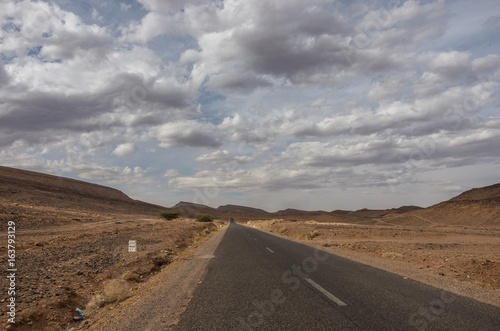 Road through Morocco steppe landscape with trees and mount at background. Area between Atlas mountains range and Sahara desert.