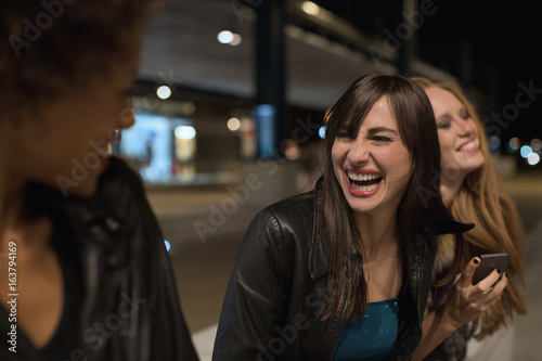 Three female friends sitting outside train station laughing before going out clubbing in the evening photo