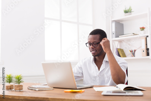 Happy black happy businessman in office, work with laptop, wearing glasses
