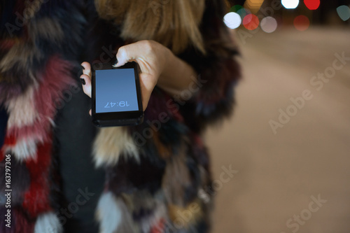 Close up of woman's hand wearing multicolour fur holding mobile phone