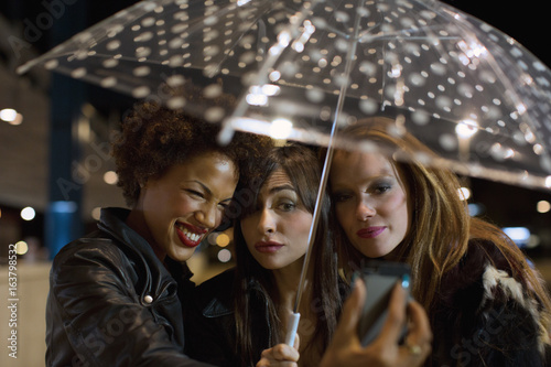 Girl friends going out at night under cute umbrella taking selfie photo