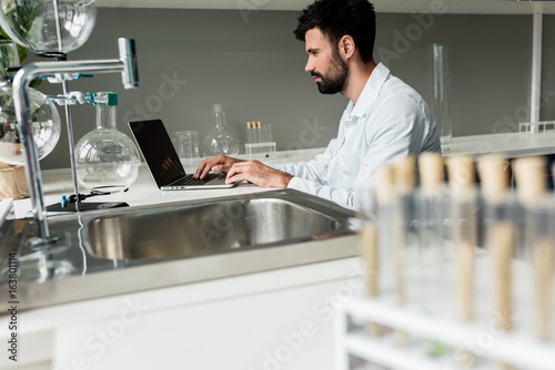 Side view of concentrated professional chemist using laptop in laboratory