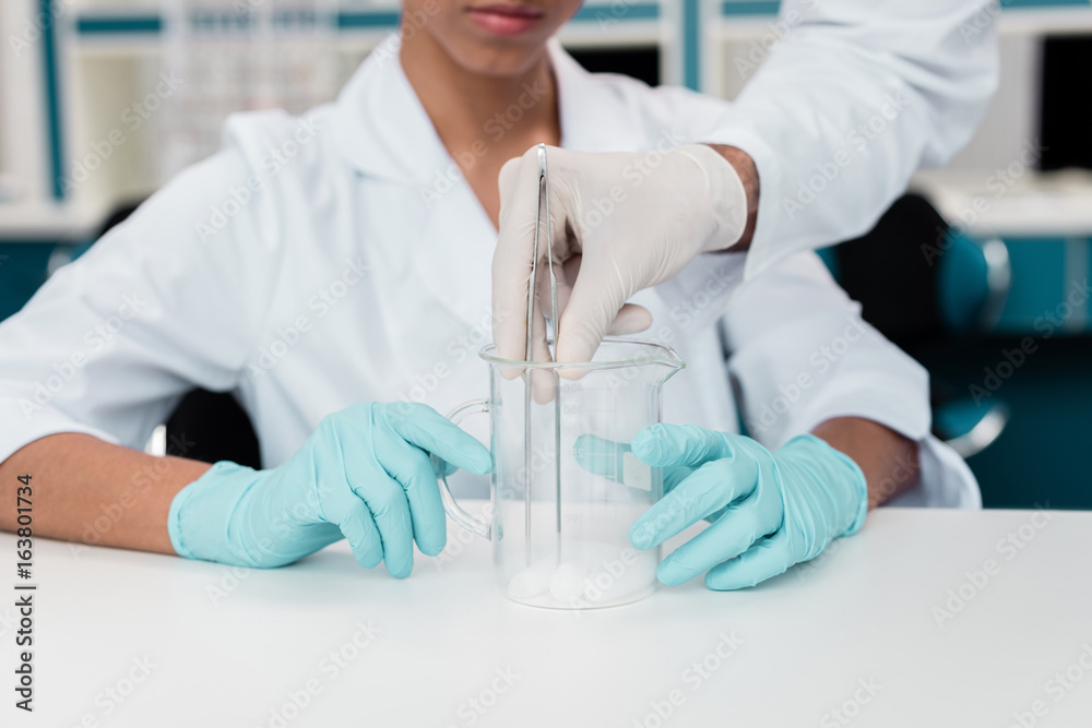 Cropped shot of colleagues in white coats working with reagent in chemical lab Cropped shot of colleagues in white coats working with reagent in chemical lab