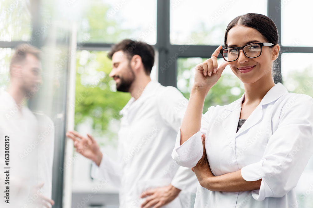 Team of professional scientists in white coats smiling while standing in laboratory Team of professional scientists in white coats smiling while standing in laboratory