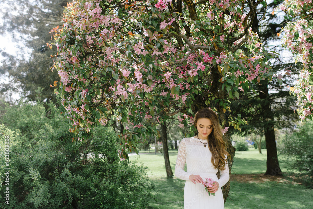 Young beautiful girl walking in a beautiful park among the flowering trees Young beautiful girl walking in a beautiful park among the flowering trees