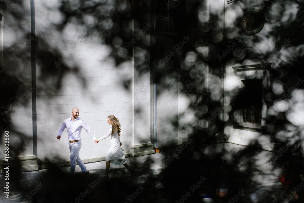Young, beautiful bride and groom walking along the street in the city Young, beautiful bride and groom walking along the street in the city