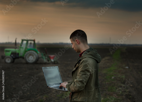 Farmer with laptop in front of tractor