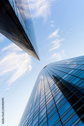 Low angle view of skyscrapers and glass buildings with blue sky in a geometric arrangement.