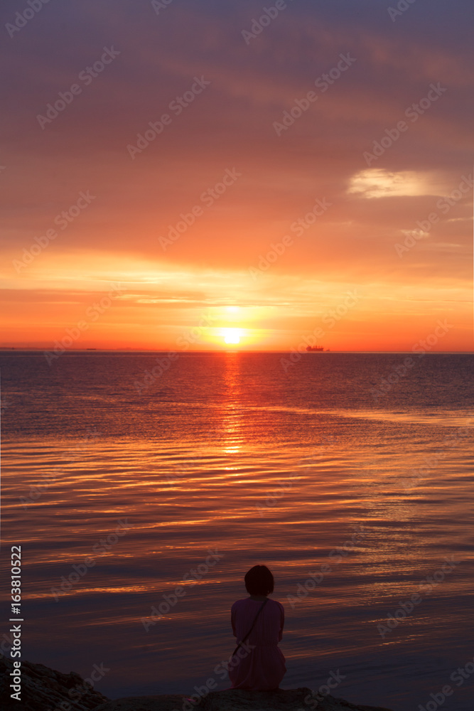 Lonely girl sitting on the beach and meets the dawn