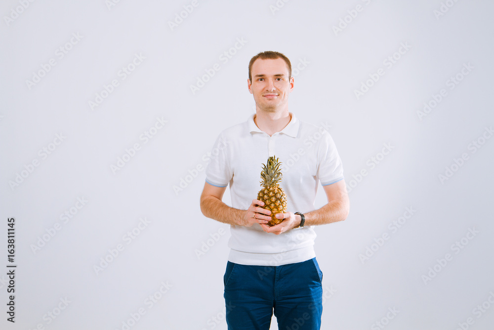 Cheerful and emotional guy holding a pineapple in his hand on a white background Cheerful and emotional guy holding a pineapple in his hand on a white background