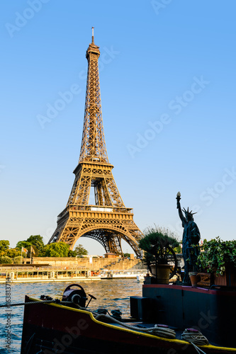 The Eiffel tower seen from the Debilly pier at sunset with a replica of the Statue of Liberty on a houseboat in the foreground.