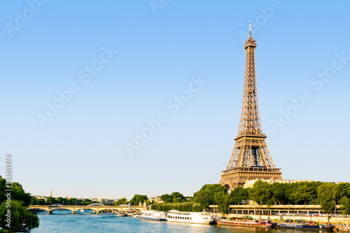 The Eiffel tower seen from the Bir-Hakeim bridge at sunset with the river Seine and tourist shuttles in the foreground.