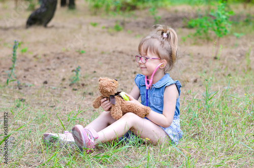 A little girl treats her teddy bear in a forest glade a copy of the free space. Summer vacation in nature.