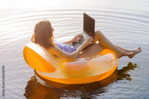 Business woman working on a laptop in an inflatable ring in the water, a copy of the free space. Workaholic, work on vacation.