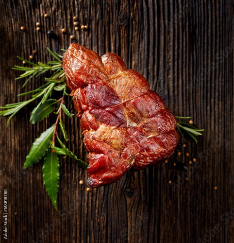 Smoked ham on a wooden rustic table with addition of fresh aromatic herbs, top view.  Natural product from organic farm, produced by traditional methods