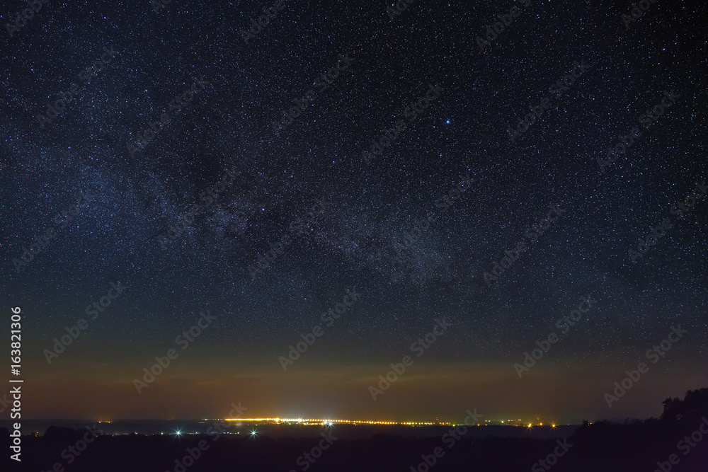 Starry night sky with the Milky Way over the city with lighting.