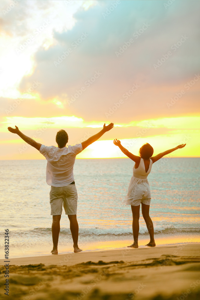 Sunset beach couple praising freedom with open arms up to the sky in success. Mindfulness, spirituality, faith, carefree people winning with raised hands concept.