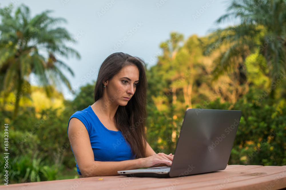 Young female freelancer working at project on her laptop in tropical park Young female freelancer working at project on her laptop in tropical park