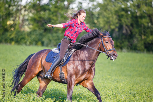 Happy young woman riding galloping horse at sunny summer day. Freedom equestrian concept image