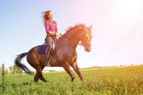 Young happy girl enjoying riding horse on green field at sunny day