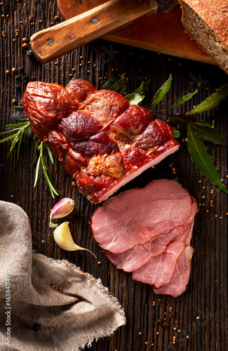 Smoked ham sliced on a wooden rustic table with addition of fresh aromatic herbs, top view. photo
