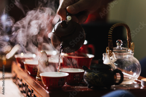 Tea ceremony. The man pours hot water from the teapot into the red chinese tea cup
