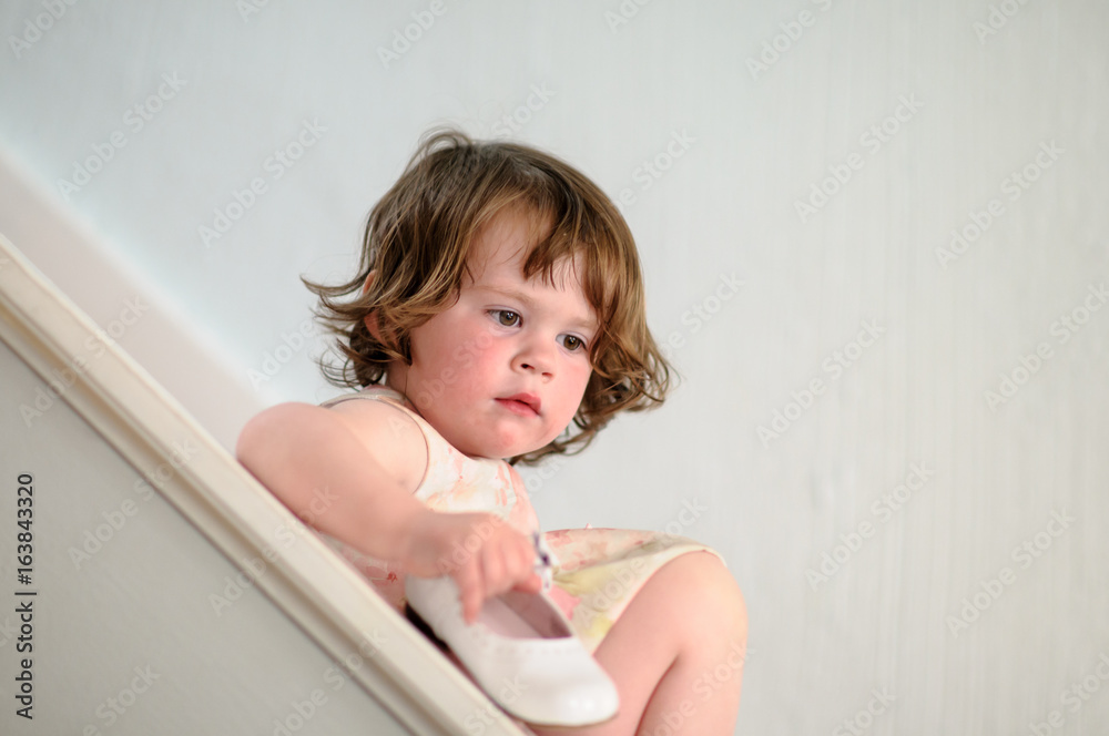 Portrait of a cute little girl inside on stairs holding dress show Portrait of a cute little girl inside on stairs holding dress show