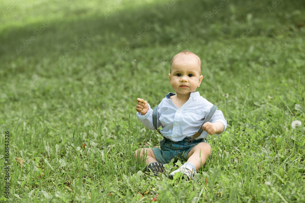 Little boy sitting on a green grass in a park with a keen look Little boy sitting on a green grass in a park with a keen look