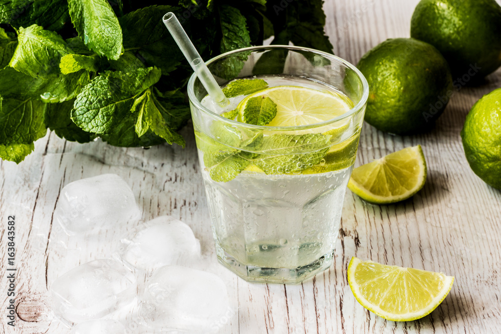 Mojito cocktail with lime, mint and ice on white wooden background.