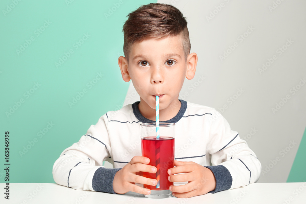 Cute little boy drinking juice while sitting at table, on color background Cute little boy drinking juice while sitting at table, on color background