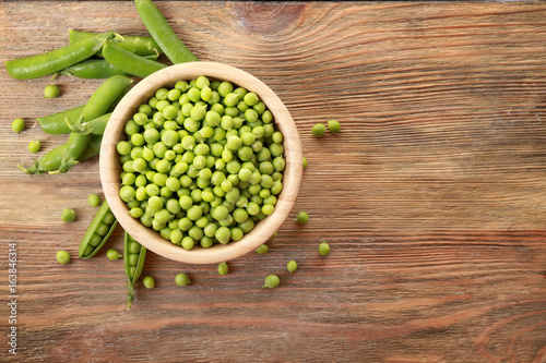 Bowl with fresh green peas on wooden background