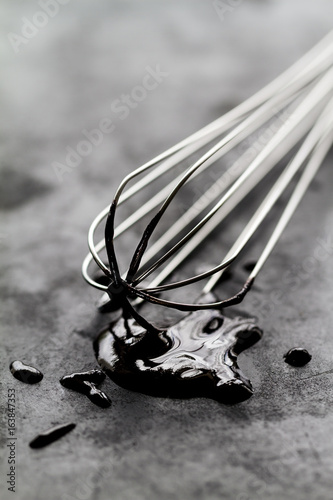 Beautiful metal baker whisk with chocolate on dark table on dark background. Closeup. Selective focus.
