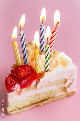 Closeup of tasty beautiful appetizing elegant piece of birthday cake with many candles. Birthday Holiday Concept.