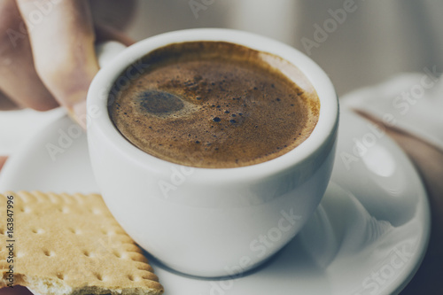 Closeup of tasty coffee espresso with tasty foam in small ceramic cup. Female hands holding warm hot drink.