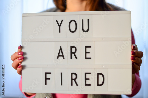 Woman holding a You are fired sign in her hands in lightbox.