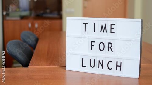 Time for lunch sign in lightbox put on the desk together with hourglass in office interior.