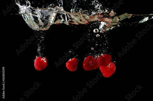 A falling fresh raspberry in water, a splash with bulbs on a black background