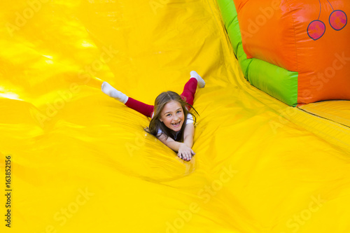 Slika na platnu Happy little girl having lots of fun on a jumping castle while sliding
