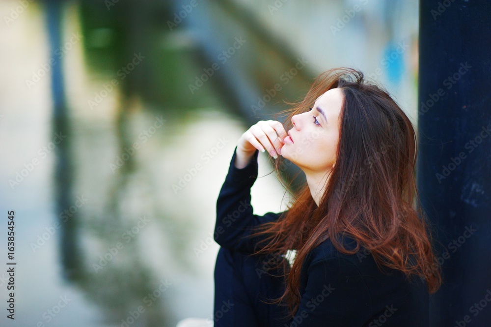 Portrait of young dreamy cute girl sitting outdoors on blurred background  of street, thoughtfully fingering a strand of hair. Side view closeup.  Stock Photo | Adobe Stock