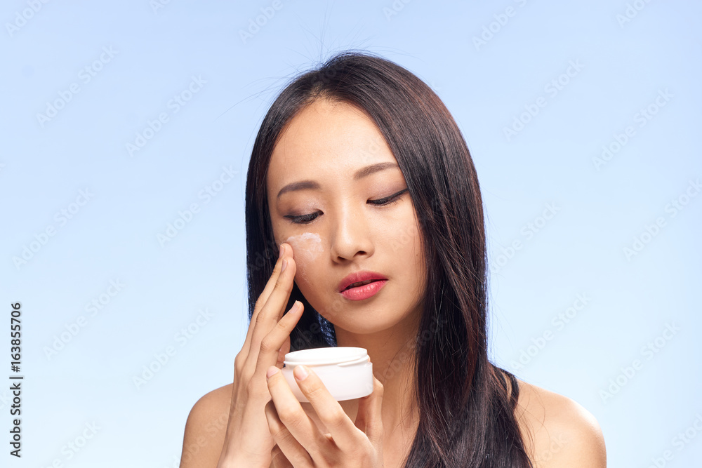 Beautiful young woman on a blue background applies cosmetic face cream, Asian Beautiful young woman on a blue background applies cosmetic face cream, Asian
