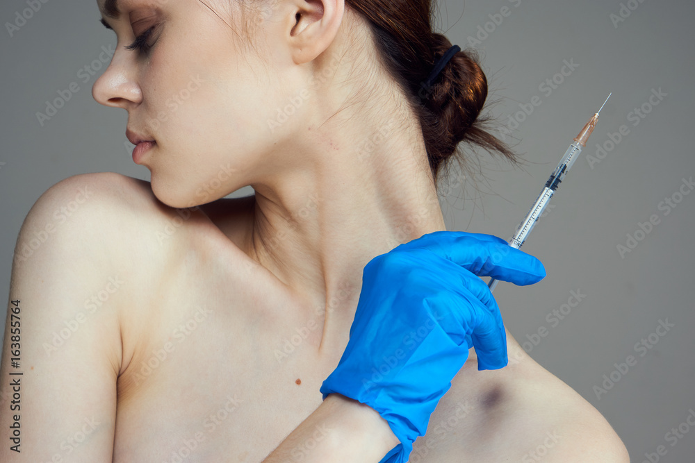 Young beautiful woman on a gray background holds a syringe, medicine, nurse