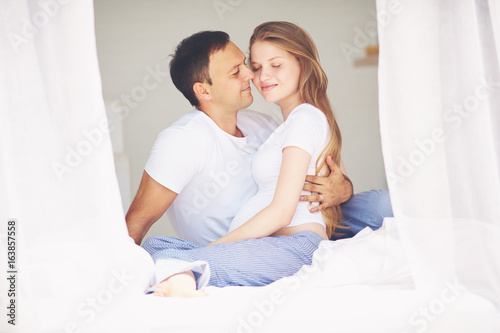 happy pregnant couple embracing in bedroom in the morning