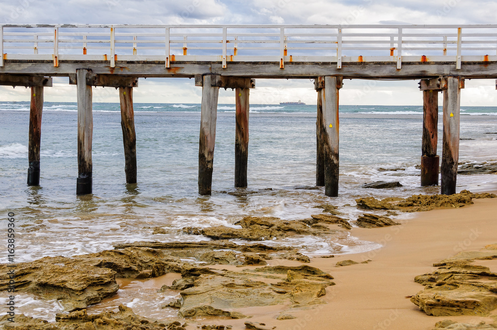 Old pillars of the Point Lonsdale Pier with a container ship on the horizon - Victoria, Australia