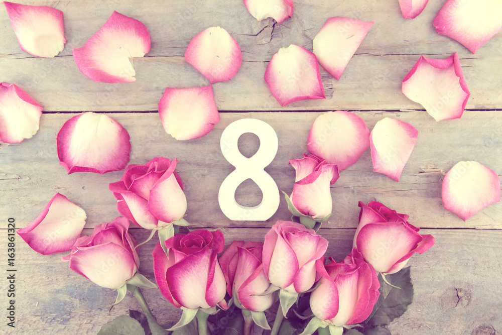Fototapeta premium Number eight as symbol of a holiday 8 march in a frame of pink roses on rustic wooden background. Greeting card with flowers for international Woman's Day. Top view.