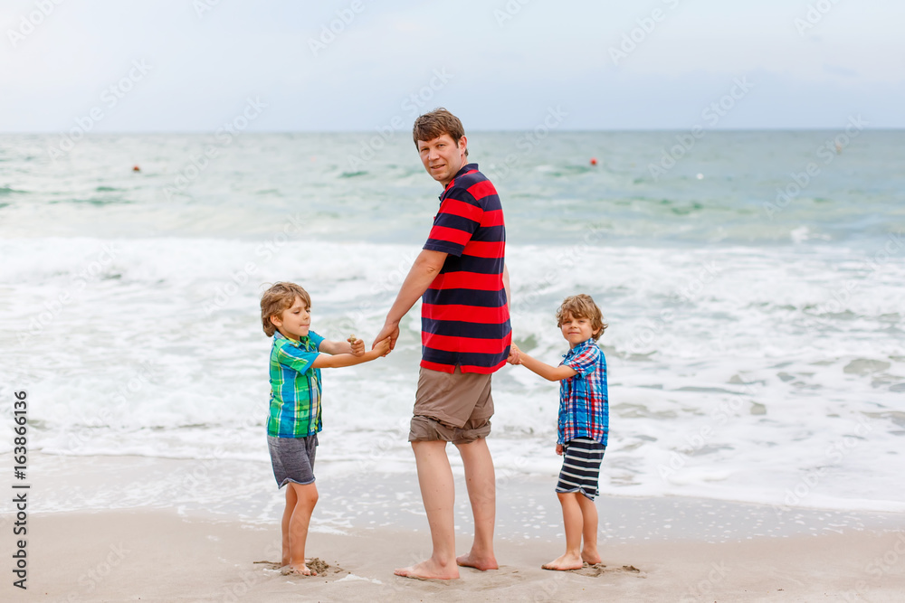 Two little kids boys and father on the beach of ocean