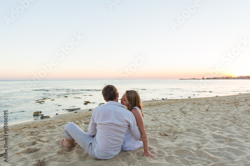Young love couple sitting together on beach, rear view