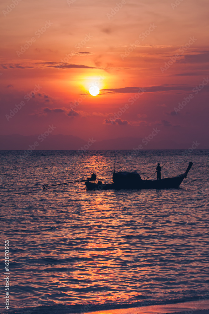 Silhouette of fisherman on boat in the sea with sunrise over horizon behind